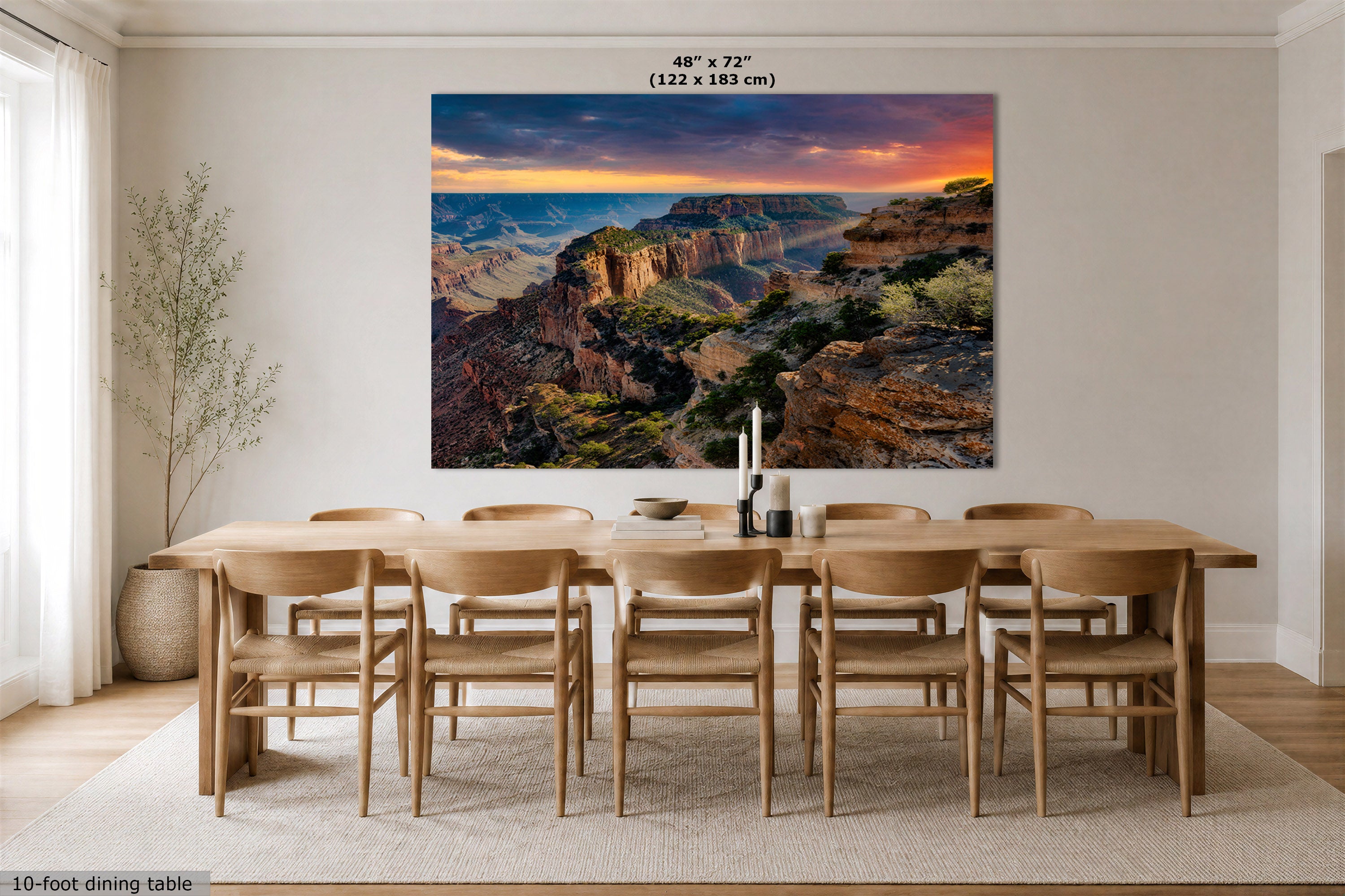 A large rectangular wall art print showing a canyon landscape with a dramatic sunset sky, displayed above a wooden dining table and chairs in a bright dining room. Small text at the top reads 48" x 72" (122 x 183 cm), and text at the bottom left says 10-foot dining table.