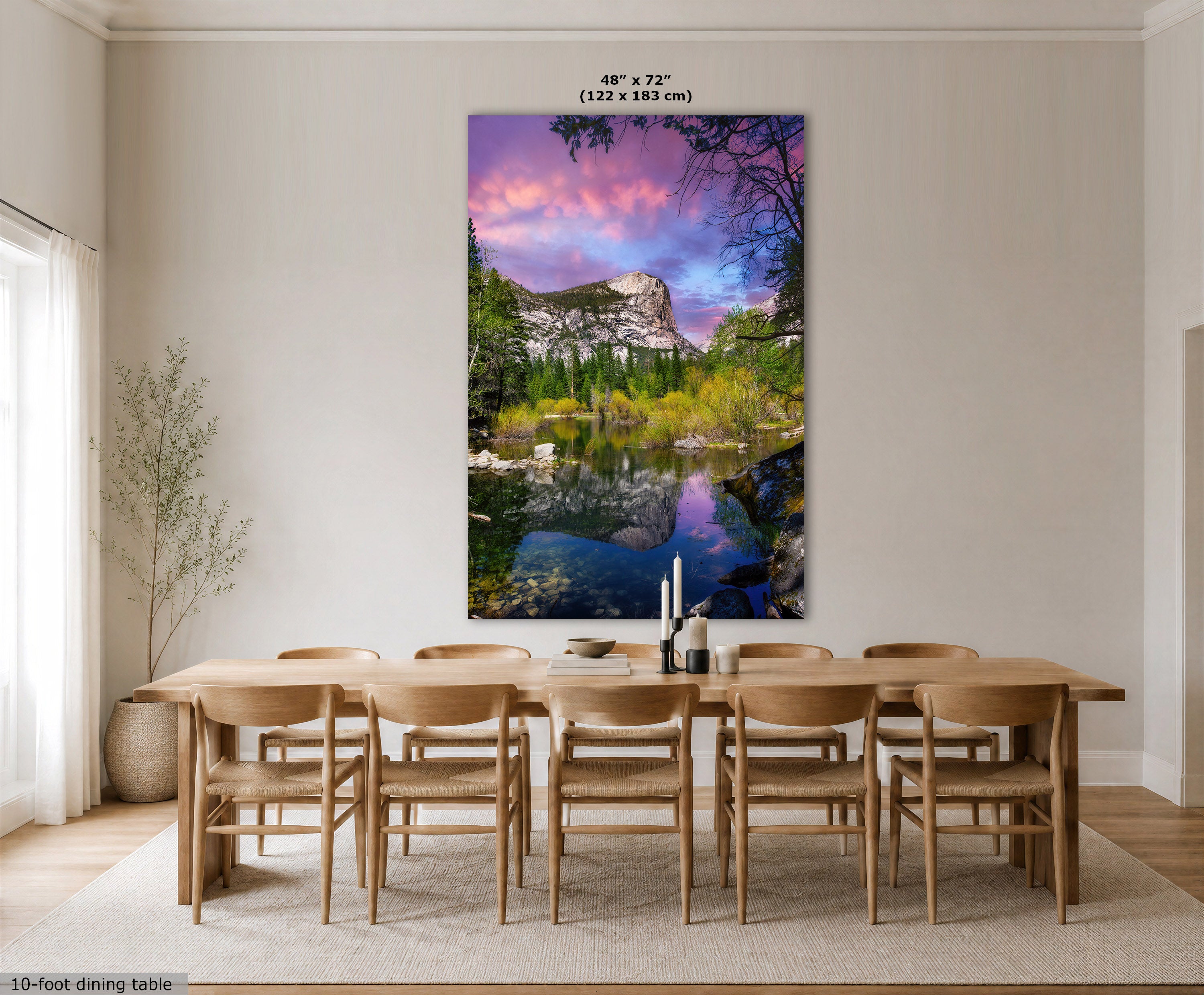 A large vertical wall art print showing a mountain lake landscape with pink and purple sky reflections, displayed above a wooden dining table and chairs in a bright modern room. Text at the top reads 48" x 72" (122 x 183 cm), and a small note at bottom left says 10-foot dining table.