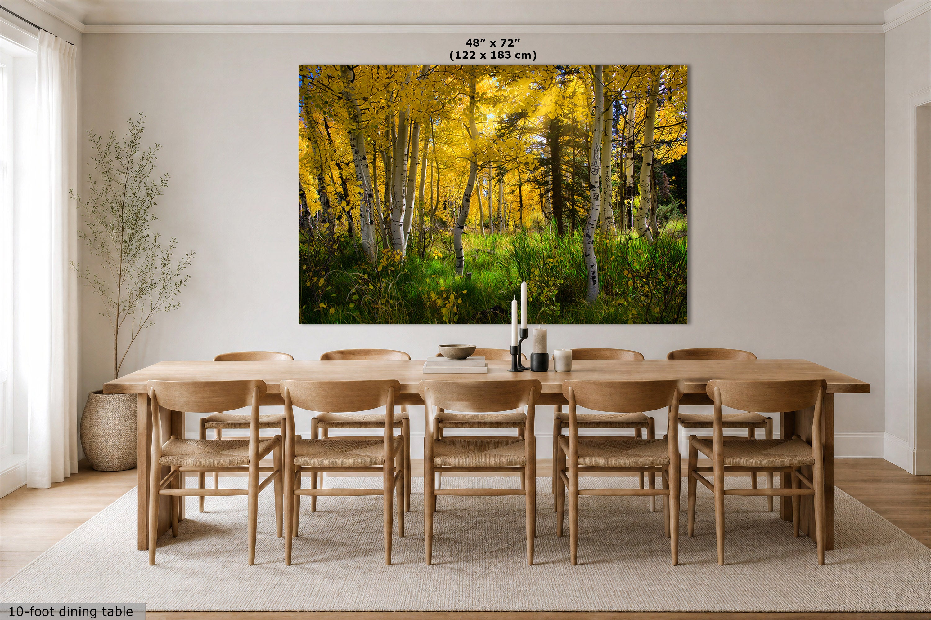 A large wall art print showing a forest of golden yellow aspen trees is displayed above a 10-foot dining table and chairs in a modern dining room. The print includes size text at the top indicating 48" x 72" (122 x 183 cm).