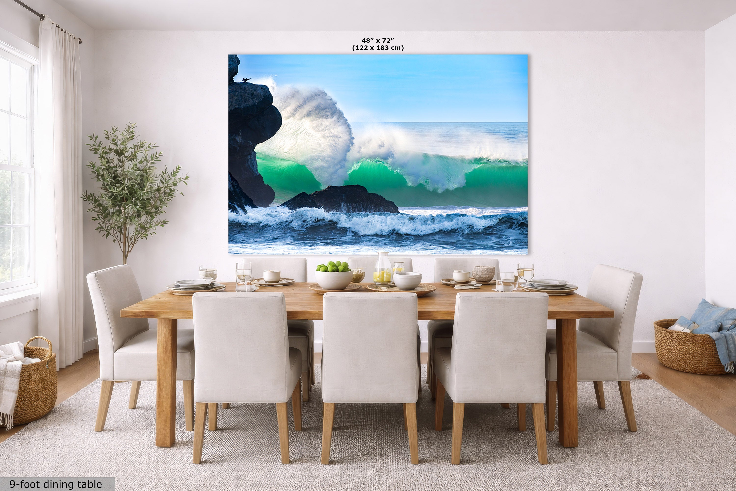 A large wall art print showing a dramatic ocean wave crashing over dark rocks under a blue sky, displayed above a dining table in a bright modern room. The print includes a size label reading 48" x 72".