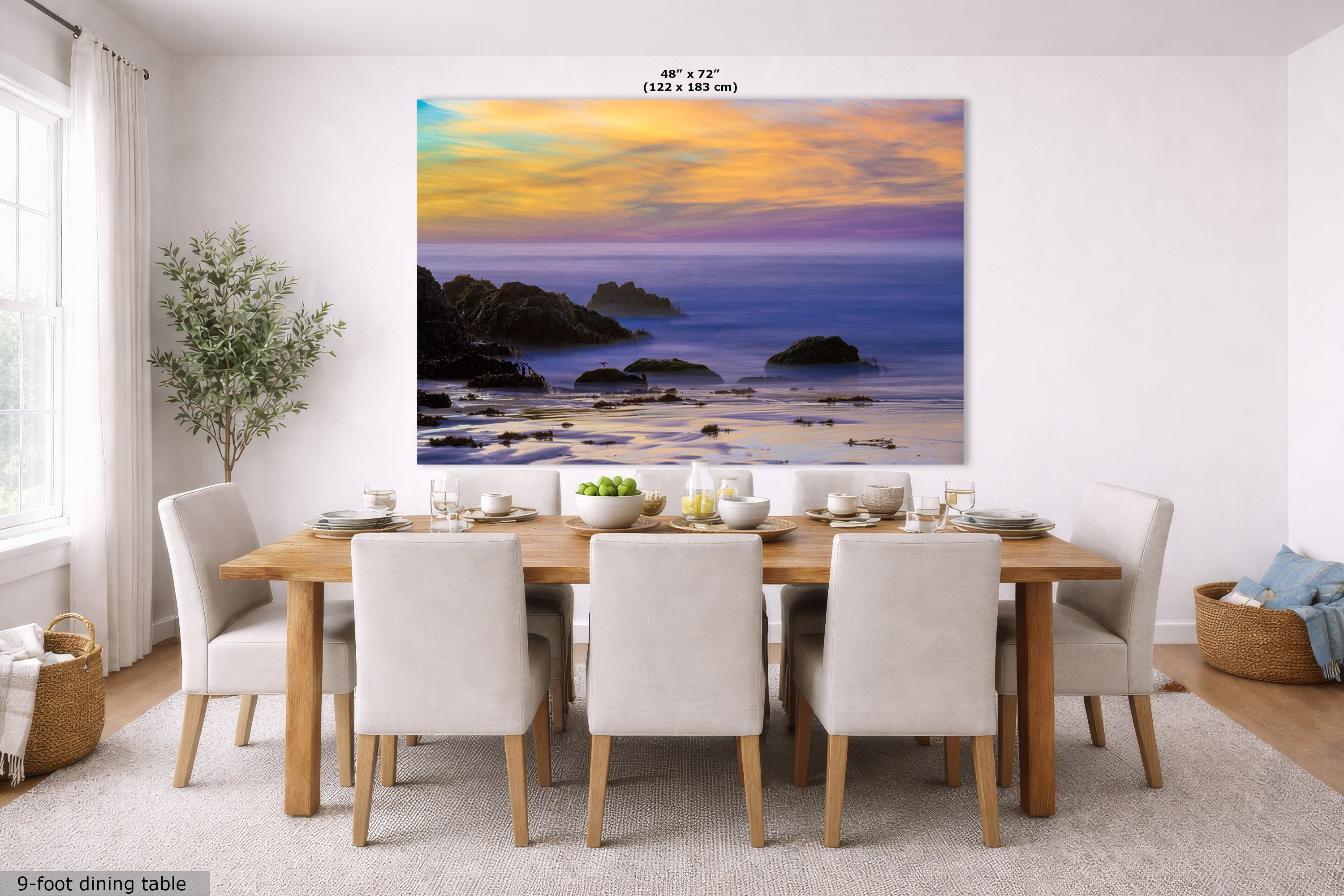 A large wall art print depicting a rocky ocean shoreline at sunset, displayed above a dining table in a bright modern dining room. The print includes a size label reading 48" x 72" (122 x 183 cm) at the top and a small note at bottom left reading 9-foot dining table.