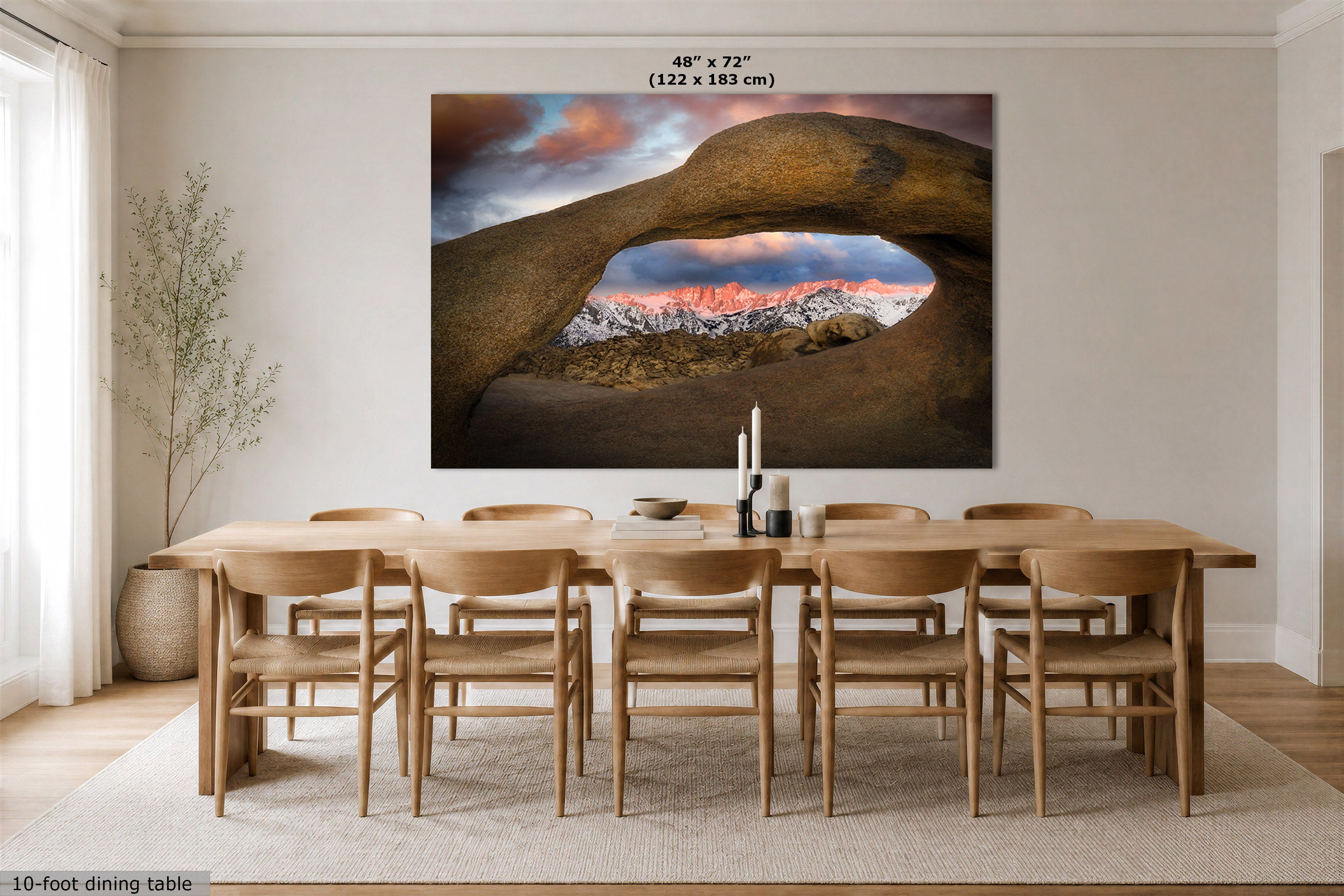 A large wall art print viewing through the Mobius Arch at the Alabama Hills, looking at the Sierra Nevada mountains at sunrise, displayed above a wooden dining table and chairs in a bright dining room. The print includes size text at the top and a small caption at the bottom left.