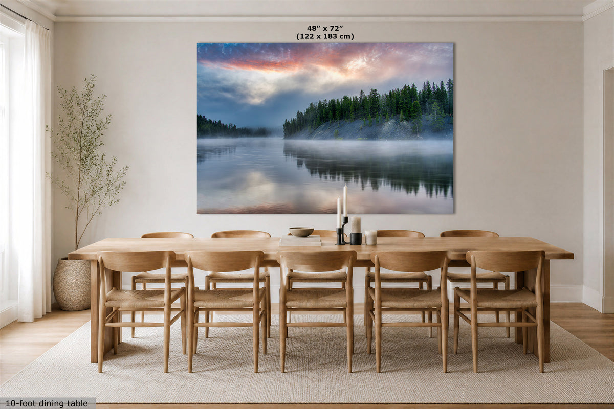 A large rectangular wall art print showing a misty lake and pine forest at sunrise, displayed above a wooden dining table and chairs in a bright neutral dining room. Text at the top reads 48 x 72" (122 x 183 cm).