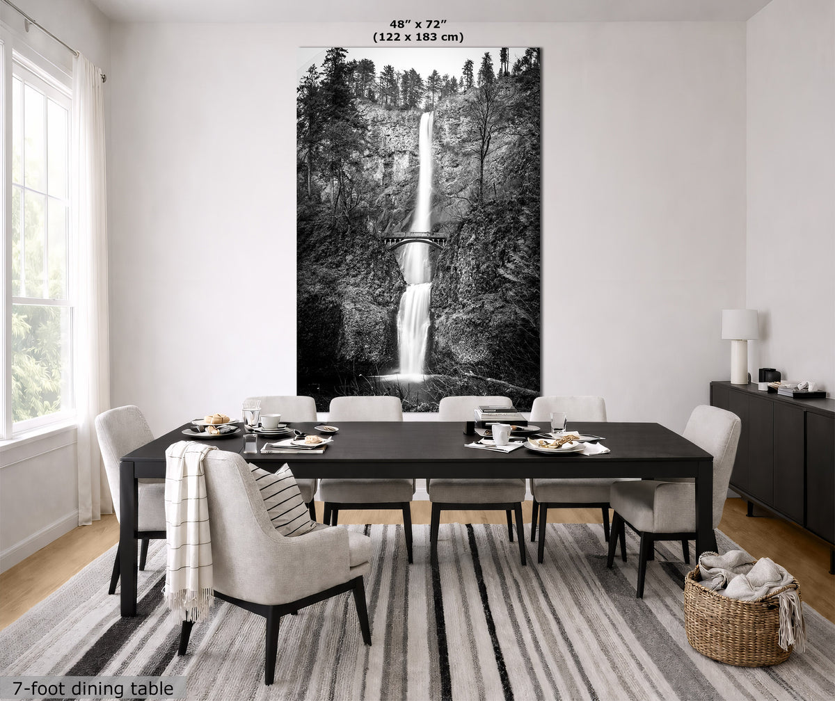 A large black and white wall art print of a waterfall in a forest is displayed above a 7-foot dining table in a modern dining room. The print includes size text at the top ('48" x 72" (122 x 183 cm)') and a width label at the bottom left ('7-foot dining table').
