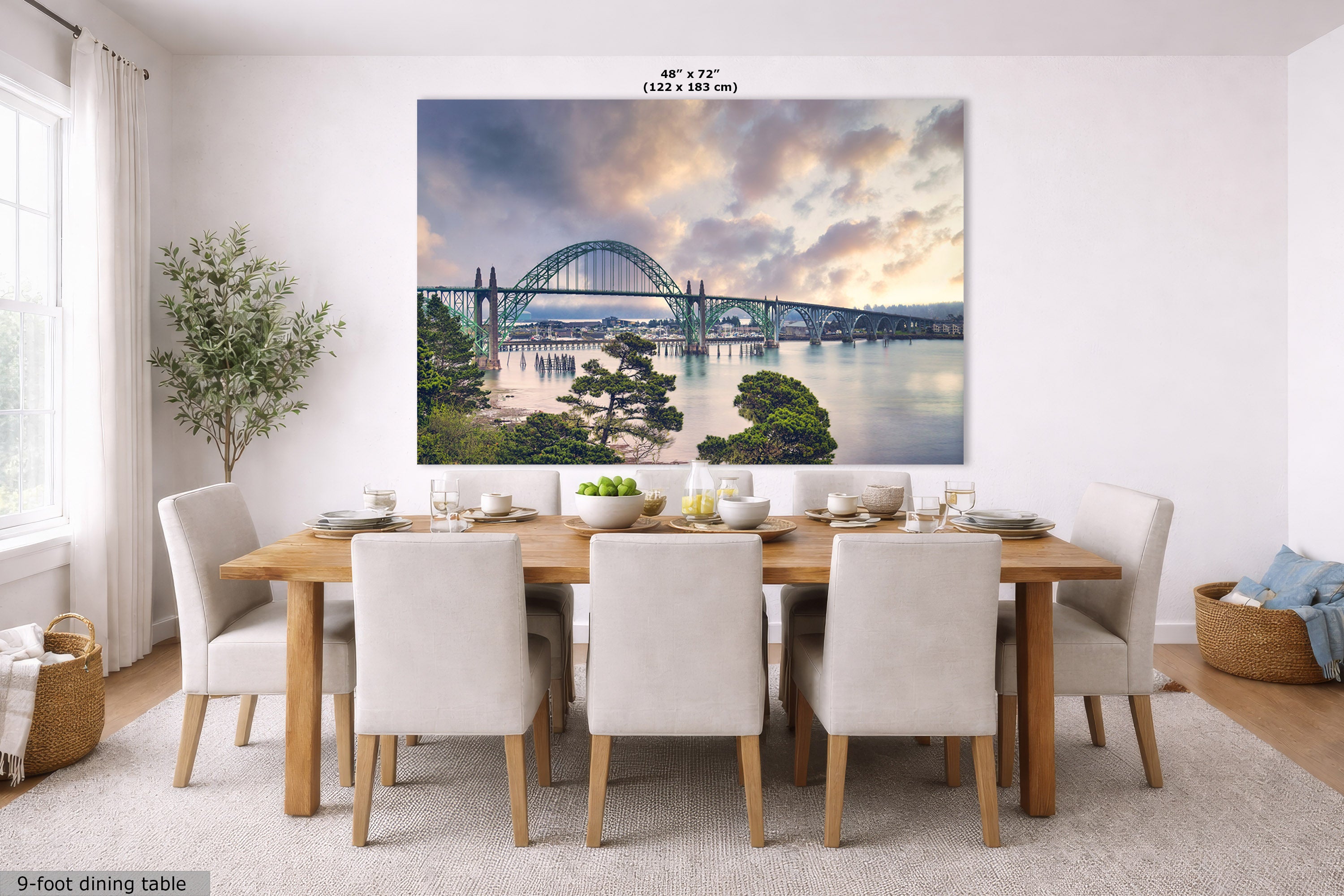 A large wall art print depicting a scenic bridge over water at sunset, displayed above a dining table in a bright modern dining room. The print includes size text at the top and a small label at bottom left reading 9-foot dining table.