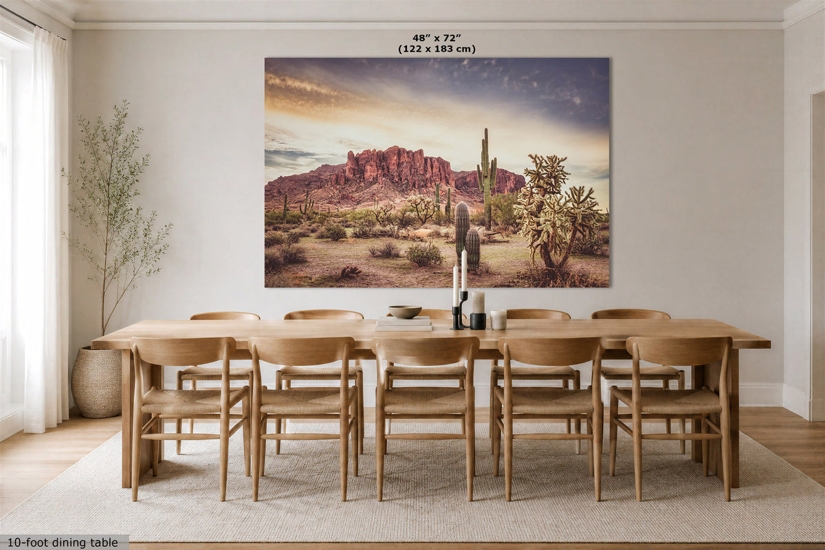 A large rectangular wall art print showing a desert landscape with red rock formations, cacti, and a dramatic sky, displayed above a wooden dining table in a bright dining room. Text at the top reads 48" x 72" (122 x 183 cm), and a small note at the bottom left says 10-foot dining table.