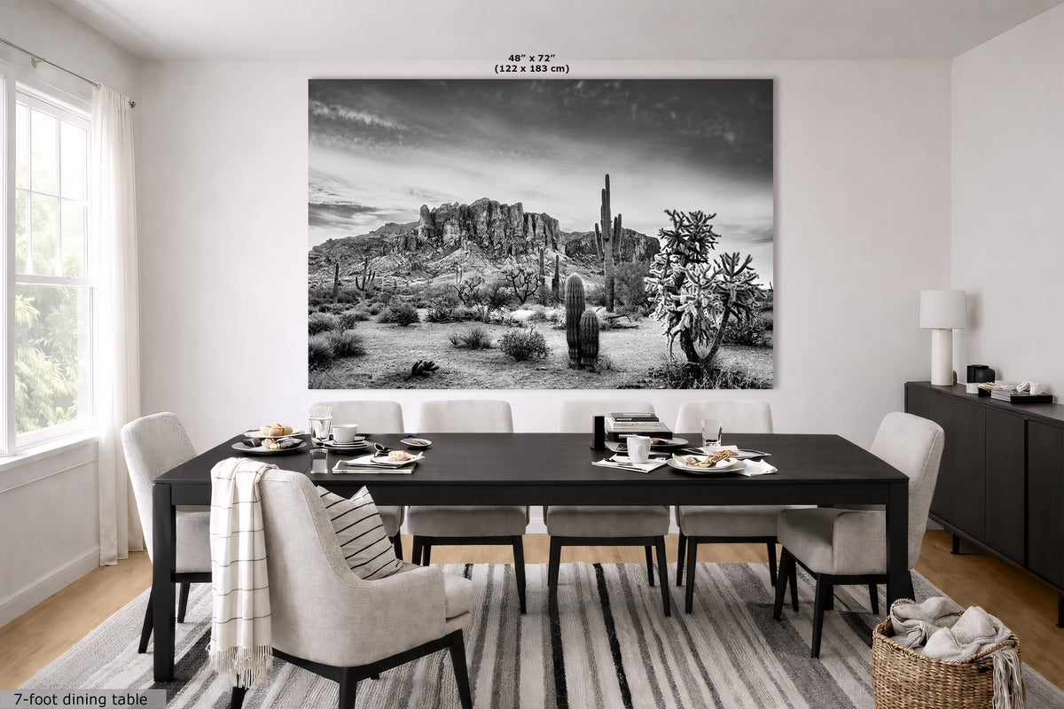 A large black and white wall art print depicting a desert landscape with cacti and rock formations, displayed above a dining table in a modern dining room setting.