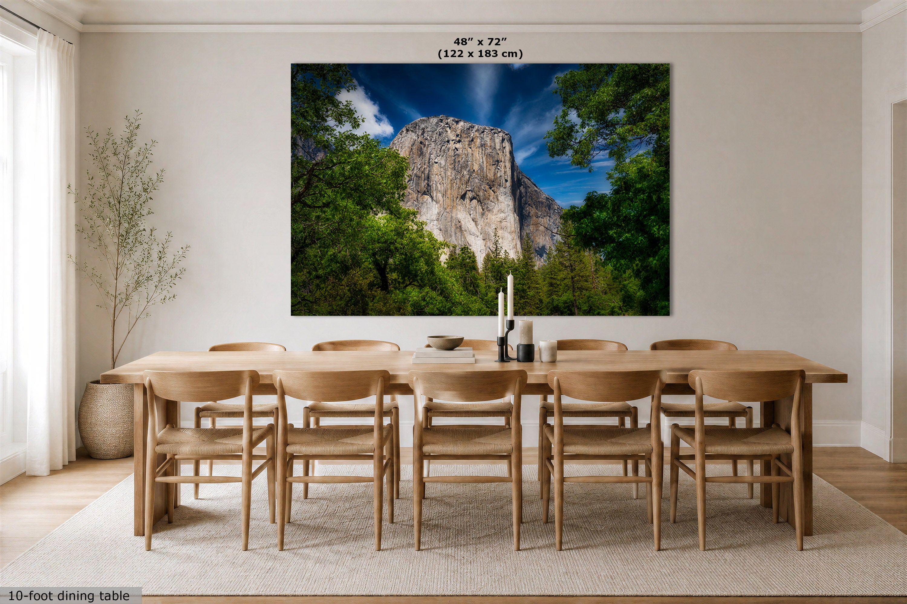 A large wall art print depicting a forested cliff landscape under a blue sky, displayed above a wooden dining table and chairs in a bright dining room. Text at the top reads 48" x 72" (122 x 183 cm), and a small note at the bottom left says 10-foot dining table.