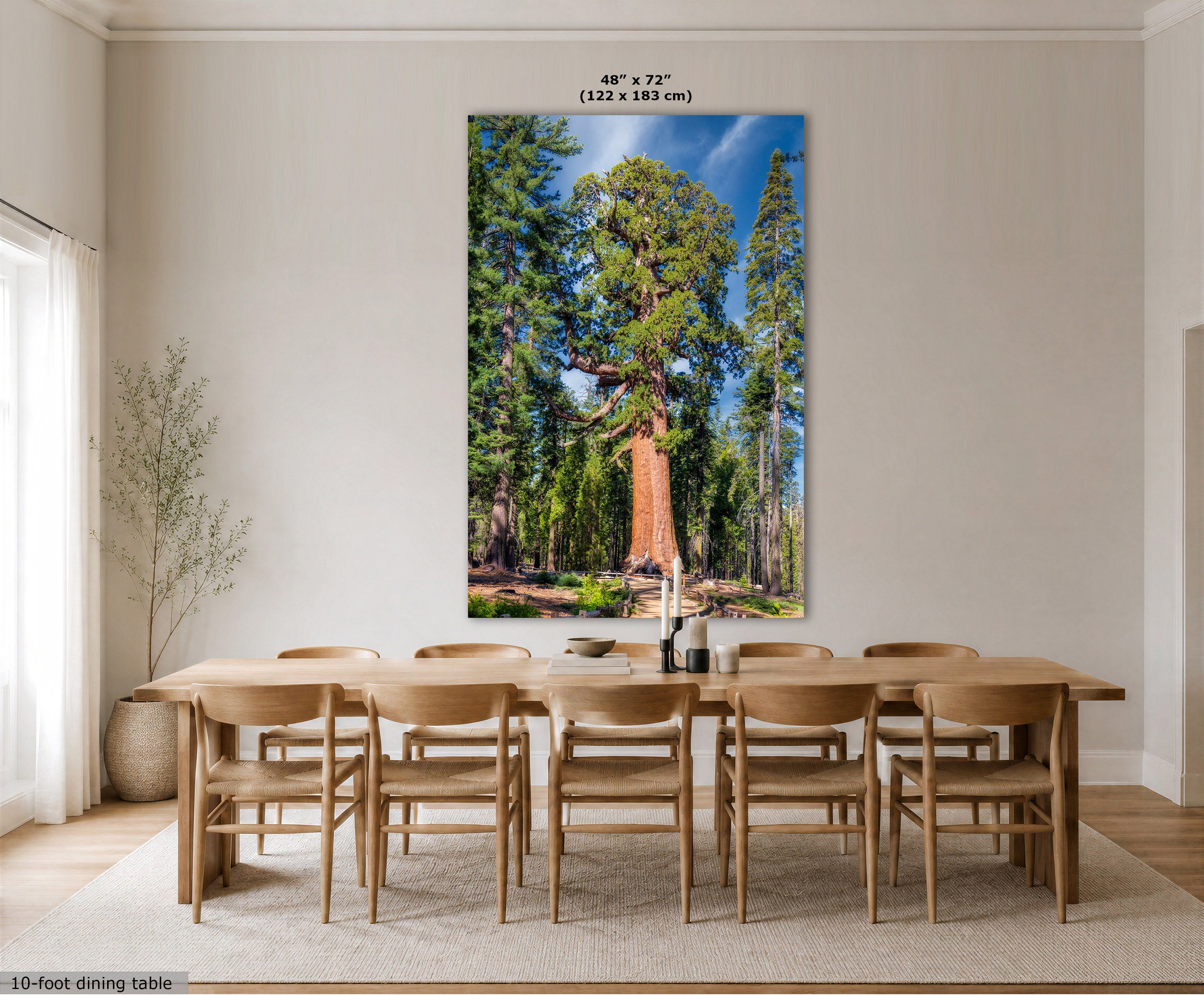 A large vertical wall art print showing a forest scene with tall trees and blue sky, displayed above a wooden dining table and chairs in a bright dining room. The print includes size text at the top and a small label at the bottom left.