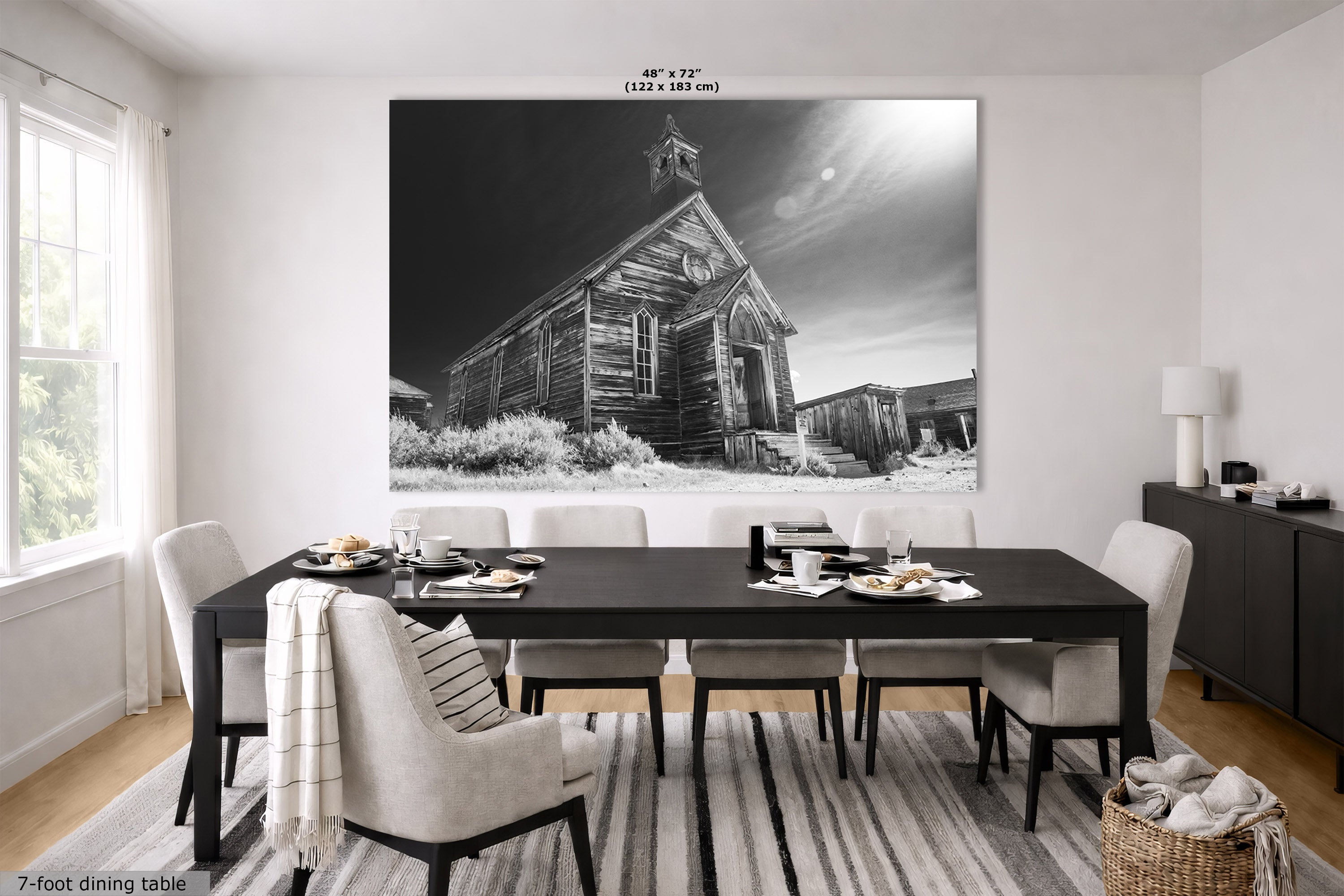 A large black and white wall art print depicting an old wooden church in Bodie Ghost Town, displayed in a modern dining room above a dark wood dining table and chairs.