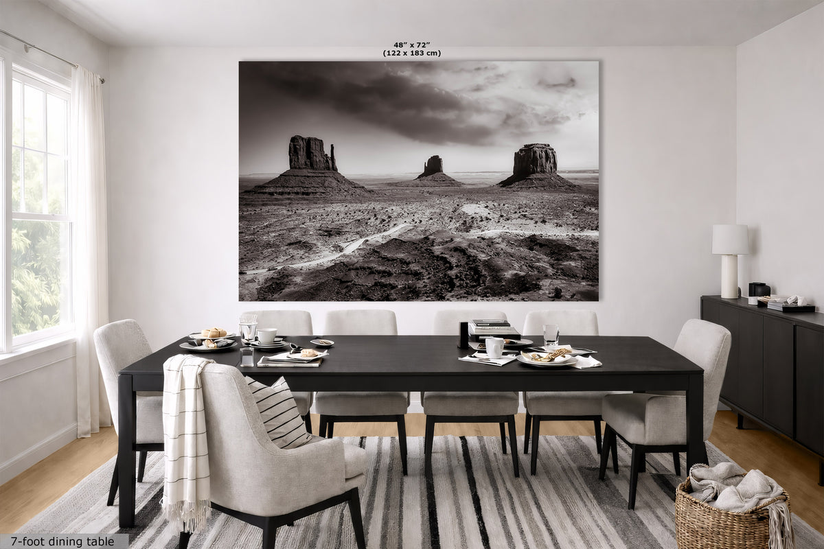 A large black and white canvas wall art print depicting Monument Valley rock formations, displayed in a modern dining room setting above a dark wood dining table and chairs.