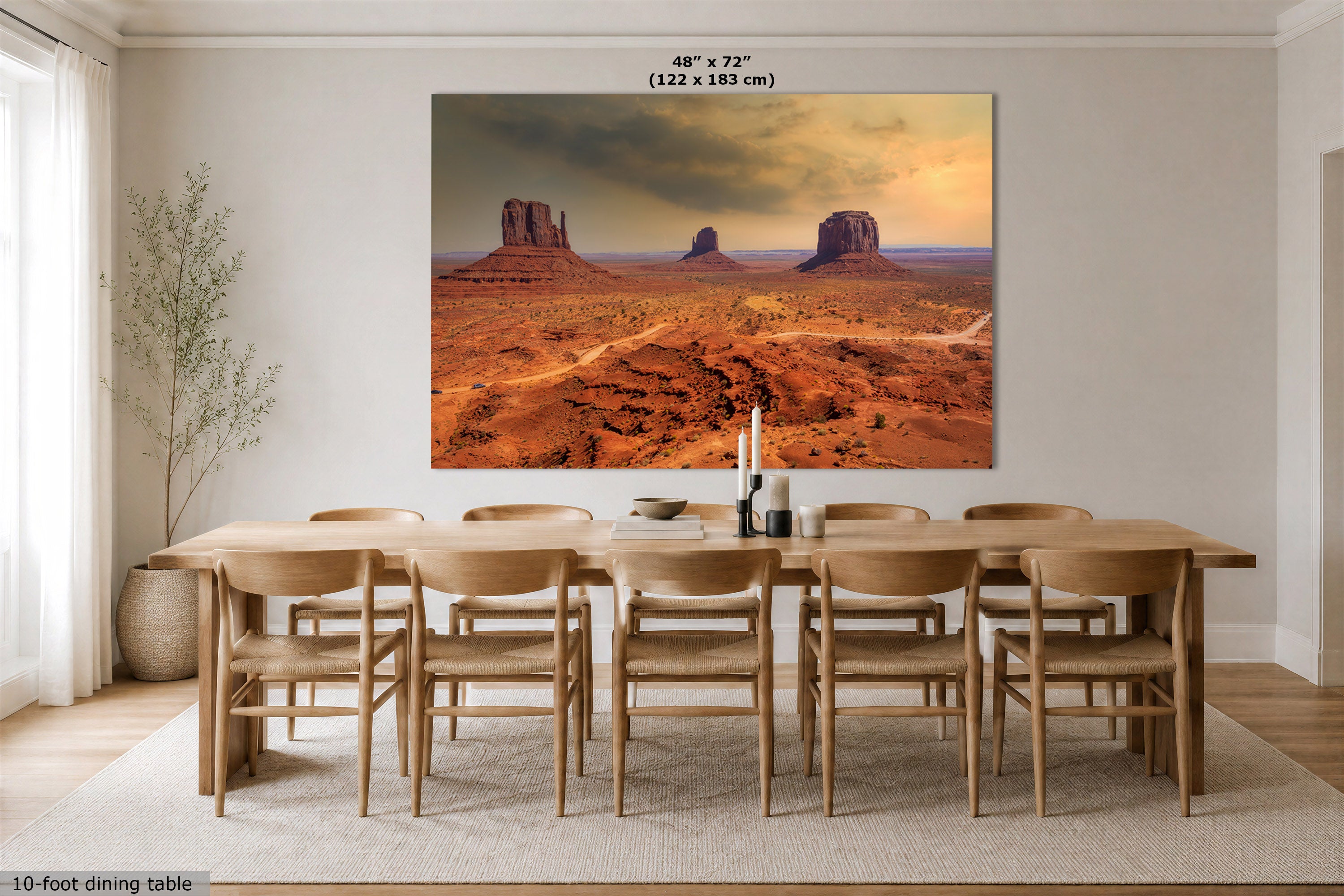A large wall art print depicting a desert landscape with red rock buttes under a dramatic sky, displayed above a wooden dining table in a modern dining room. Text at the top indicates the print size as 48" x 72" (122 x 183 cm).