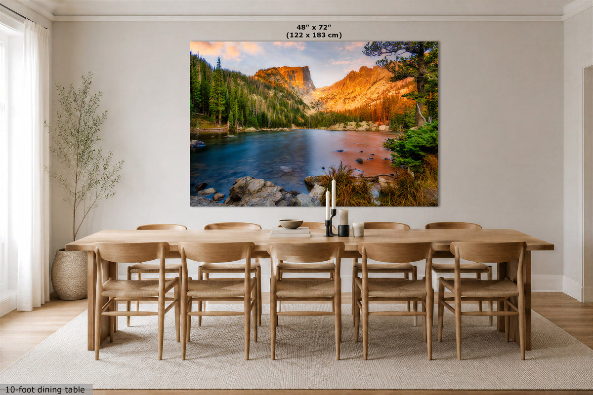 A large wall art print showing a mountain lake landscape with warm orange-brown peaks and blue water, displayed above a wooden dining table in a bright modern room. Text at the top reads 48" x 72" (122 x 183 cm).