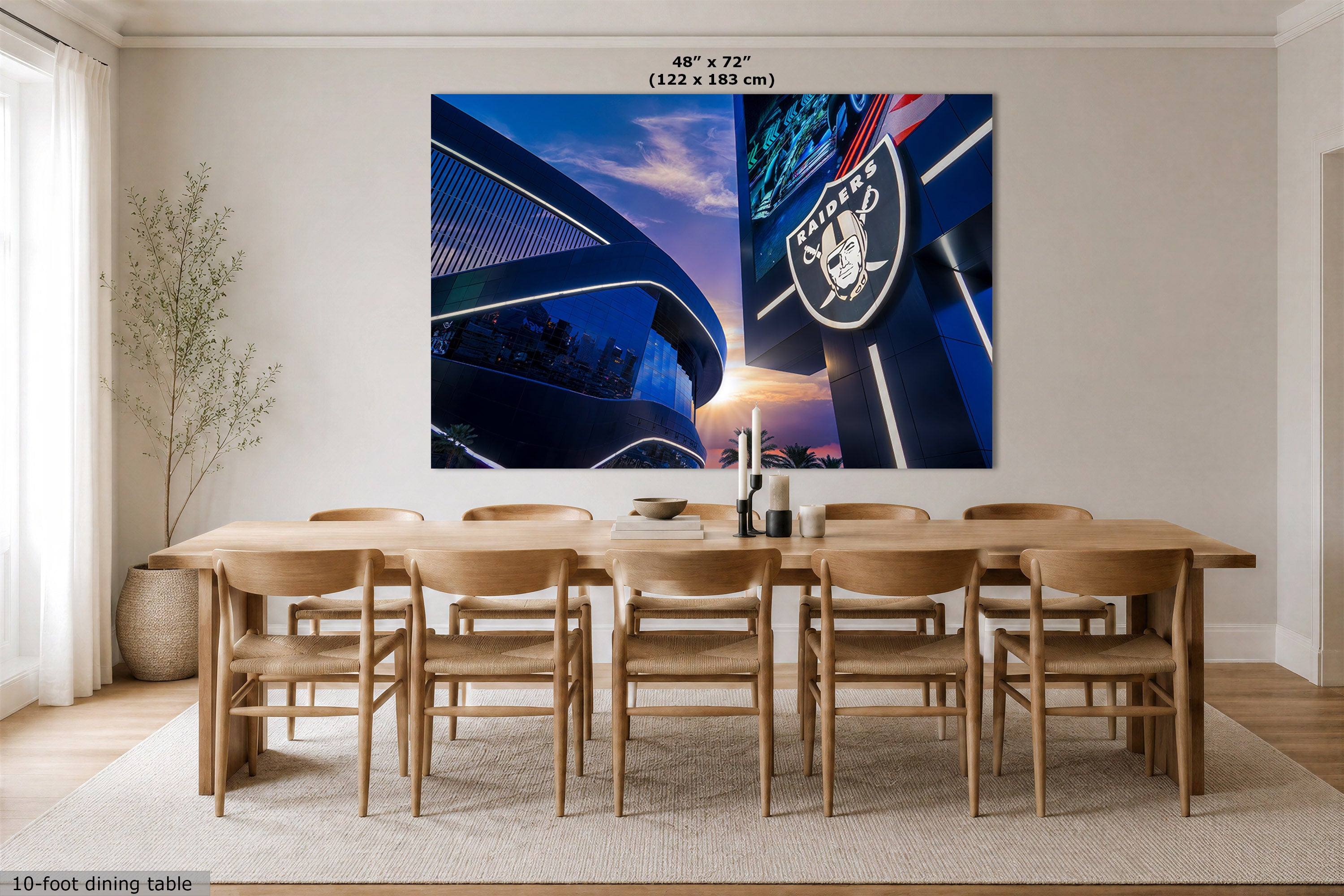 A large rectangular wall art print showing a stadium sunset scene with the Raiders logo, displayed above a wooden dining table in a bright modern dining room. Text at the top reads 48" x 72" (122 x 183 cm).
