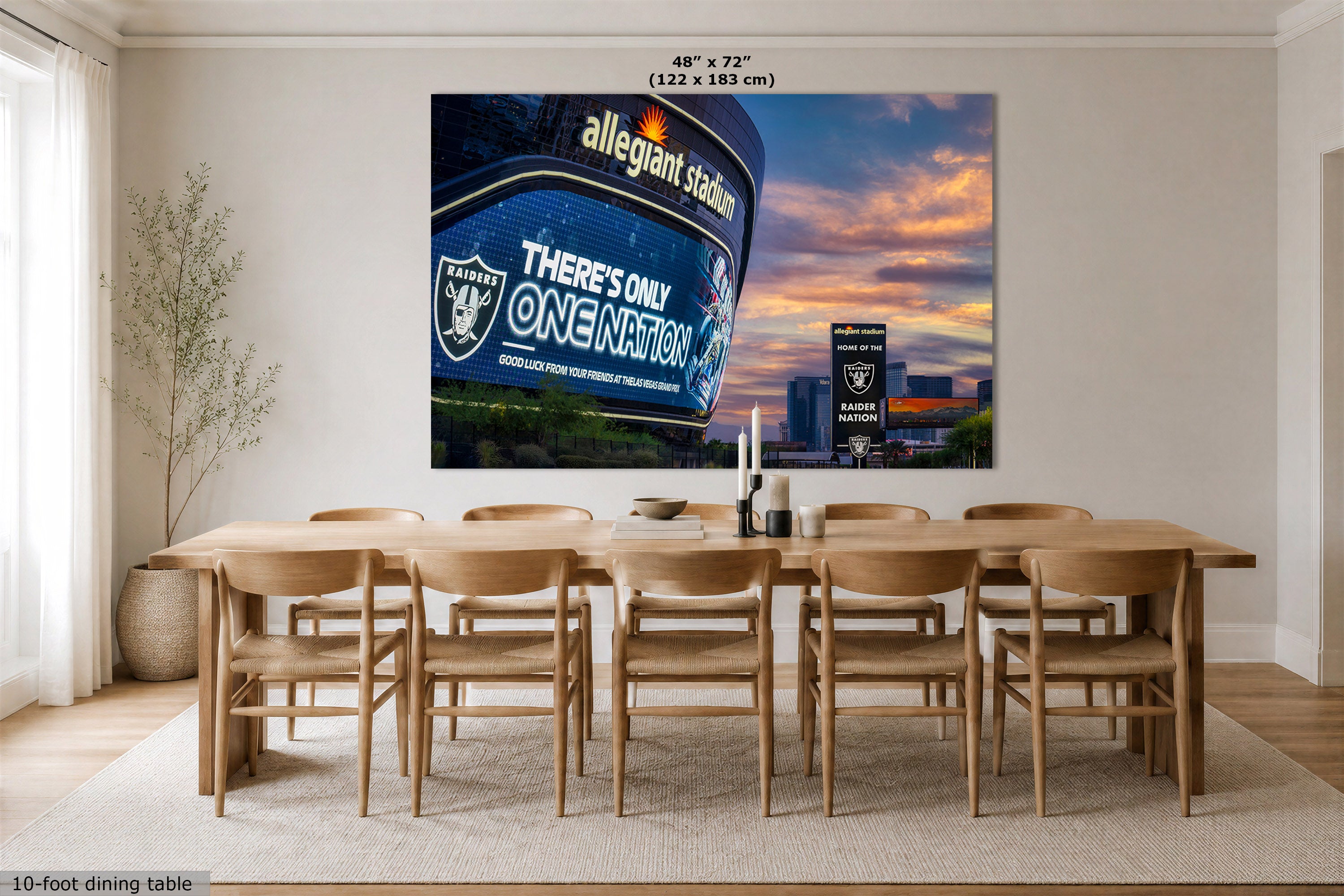 A large wall art print of the Las Vegas Raiders Allegiant Stadium at sunset, displayed in a modern dining room setting above a wooden dining table and chairs. The print features the text 'allegiant stadium' and 'THERE'S ONLY ONE NATION' with the Raiders logo.