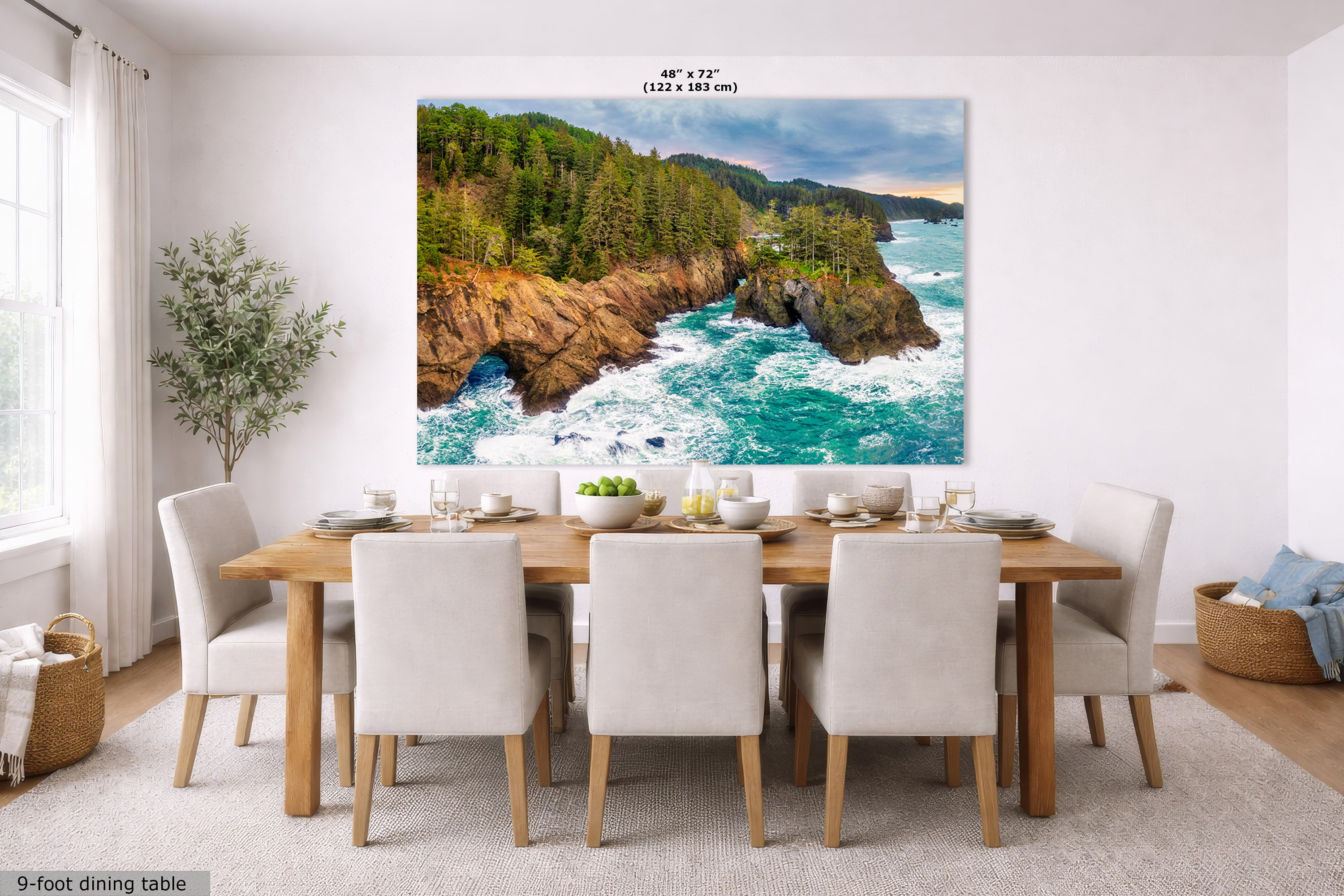 A large wall art print depicting a rocky coastline with turquoise ocean waves and a green forest, displayed above a dining table in a bright, modern room. Text at the top reads 48" x 72" (122 cm x 183 cm), and a small label at bottom left says 9-foot dining table.
