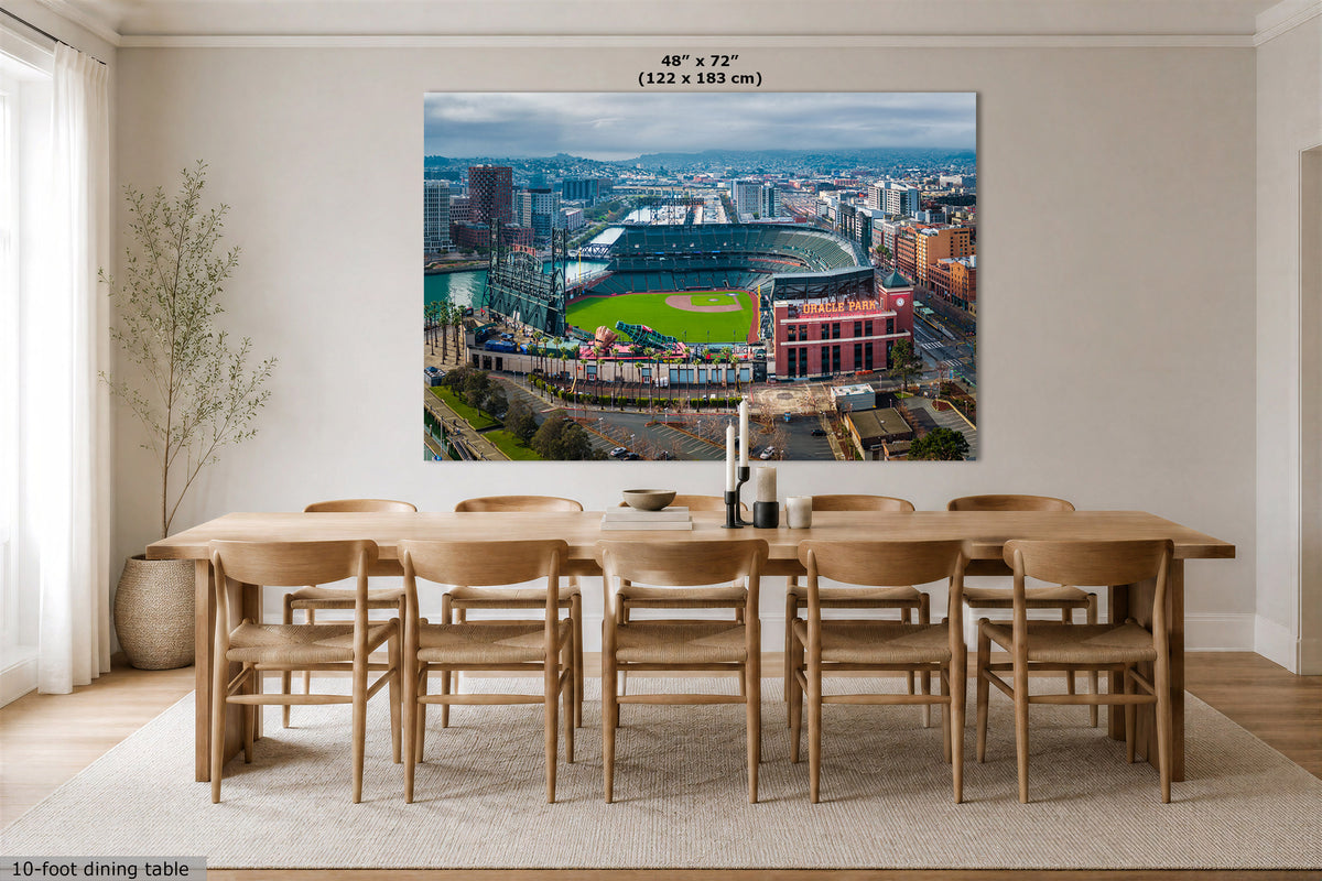 A large Oracle Park Stadium wall art print showing an aerial view of a city stadium and surrounding buildings, displayed above a wooden dining table in a bright dining room. Text at the top of the print reads 48" x 72" (122 x 183 cm).