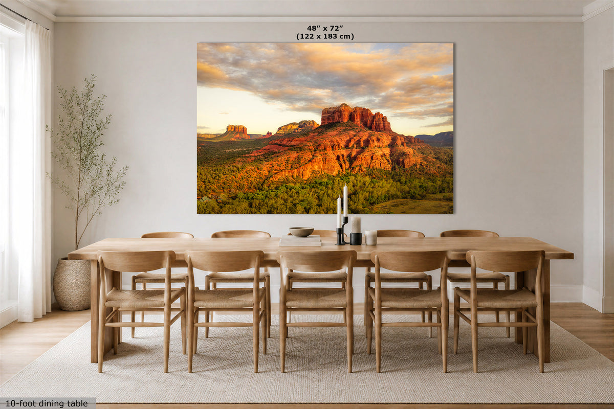 A large rectangular wall art print showing a desert rock landscape at sunset, displayed above a wooden dining table and chairs in a bright dining room. The print includes size text at the top and a small note at bottom left.