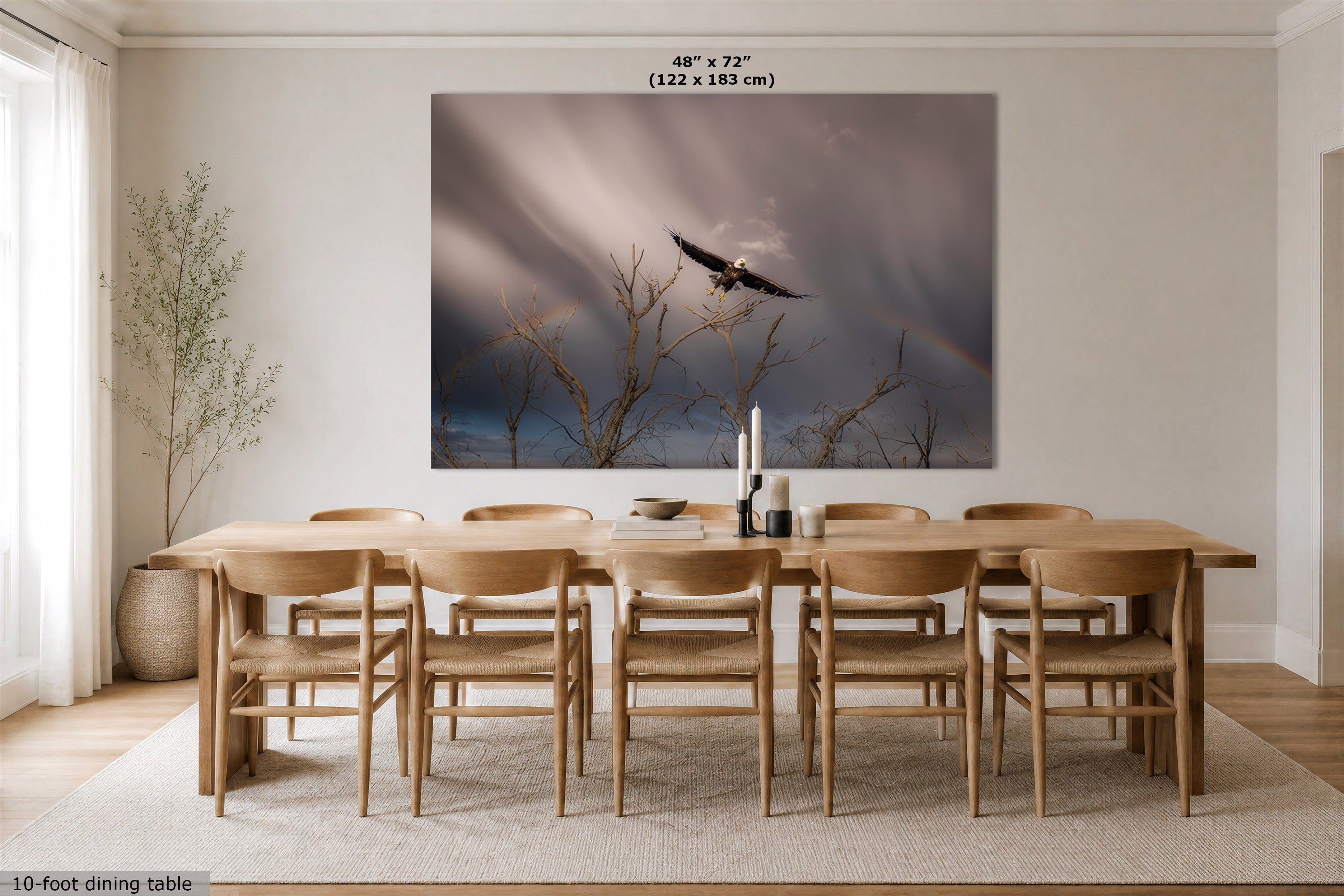 A large wall art print showing a bald eagle flying through dramatic storm clouds with a faint rainbow, displayed above a wooden dining table and chairs in a bright, modern dining room. The print includes size text at the top reading 48" x 72" (122 x 183 cm).