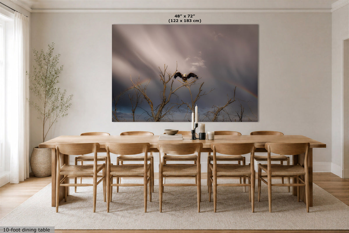 A large wall art print showing a dramatic storm sky with a bird silhouette and faint rainbow, displayed above a wooden dining table and chairs in a bright modern dining room. Text at the top indicates dimensions 48" x 72" (122 x 183 cm).