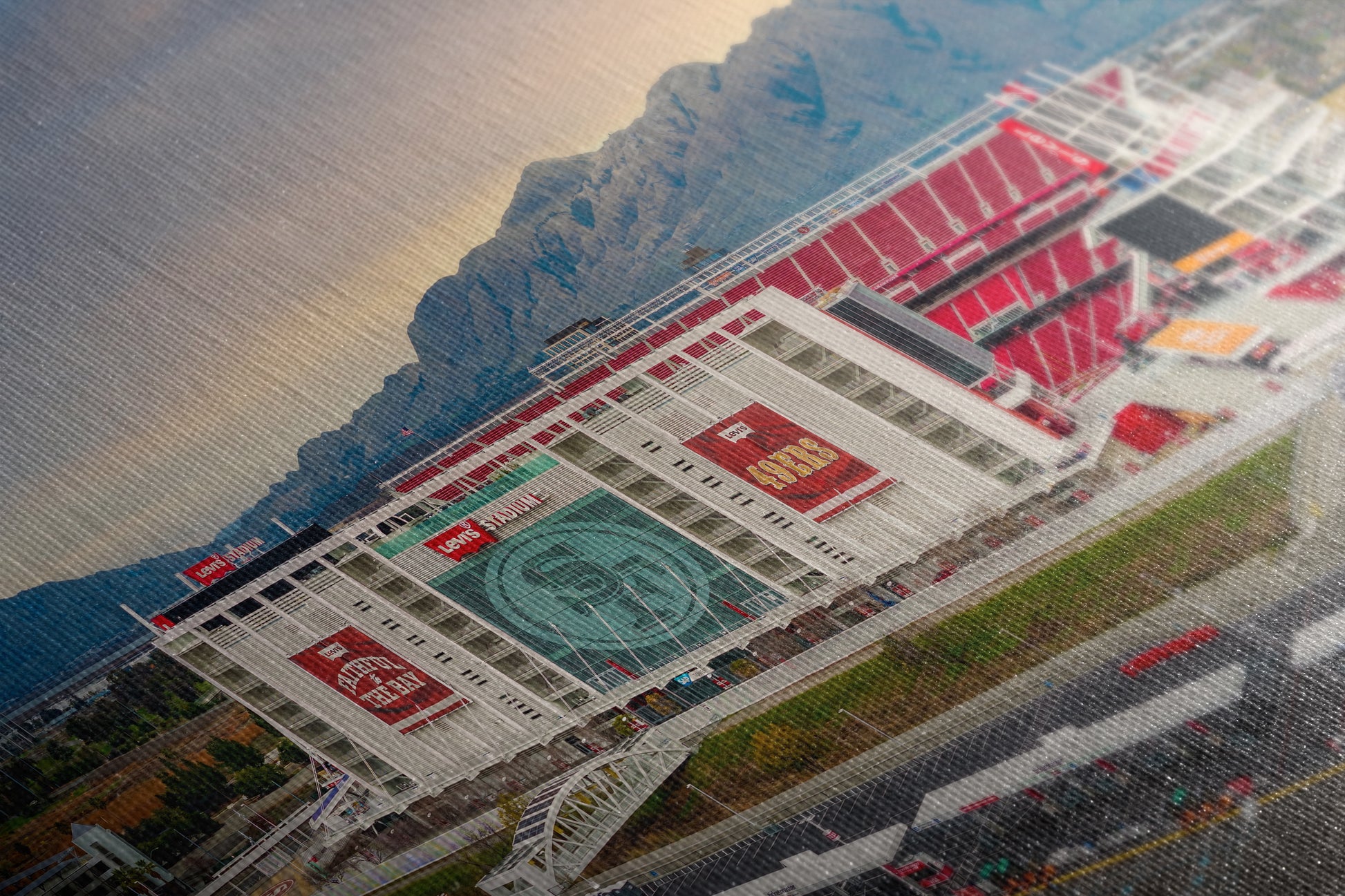 a large stadium with a mountain in the background, featuring various advertisements and signs on the exterior of the building.