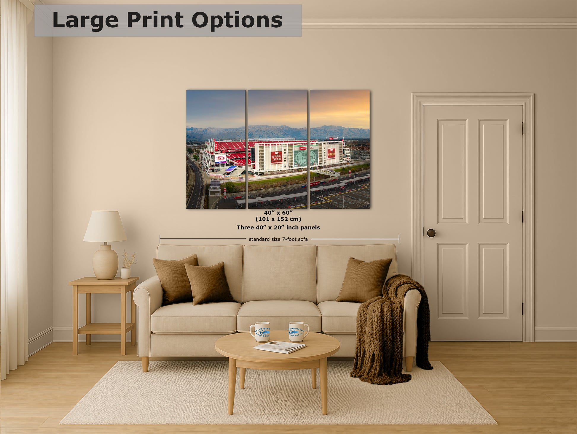 The image is a living room with a large print of a three-piece collage of a stadium or sports arena in the background, hanging on the wall above a beige sofa.