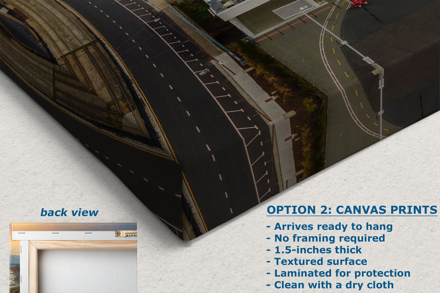 The image is a canvas print featuring an aerial view of a road with buildings and a bridge in the background. The text below the image provides information about the print, including that it is a back view of the print, arrives ready to hang, does not require framing, is 1.5-inches thick, has a textured surface, is laminated for protection, and can be cleaned with a dry cloth.