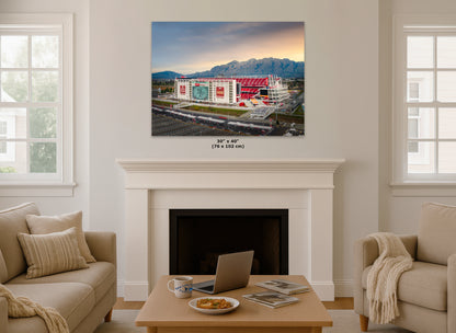 a cozy living room with a fireplace, a coffee table, and two couches. Above the fireplace, there is a large framed picture of a stadium with mountains in the background.