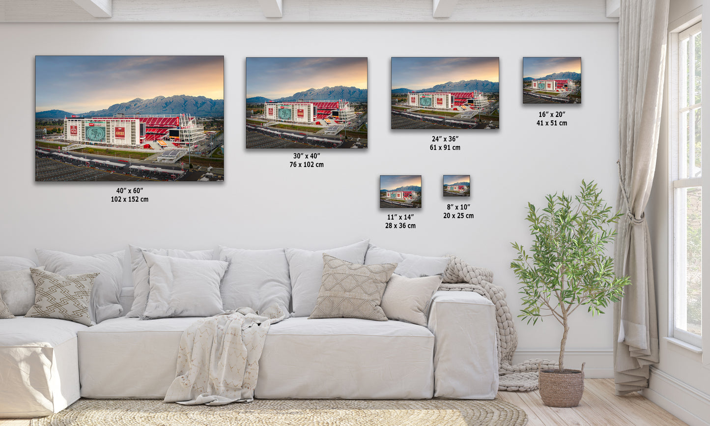 The image is a living room with a white sofa and a potted plant. There are four framed pictures of a building displayed on the wall, each with a different size and resolution. The pictures are arranged in a row, with the largest one being the tallest and the smallest one being the shortest. The wall has a white color scheme, and the room appears to be well-lit and decorated.