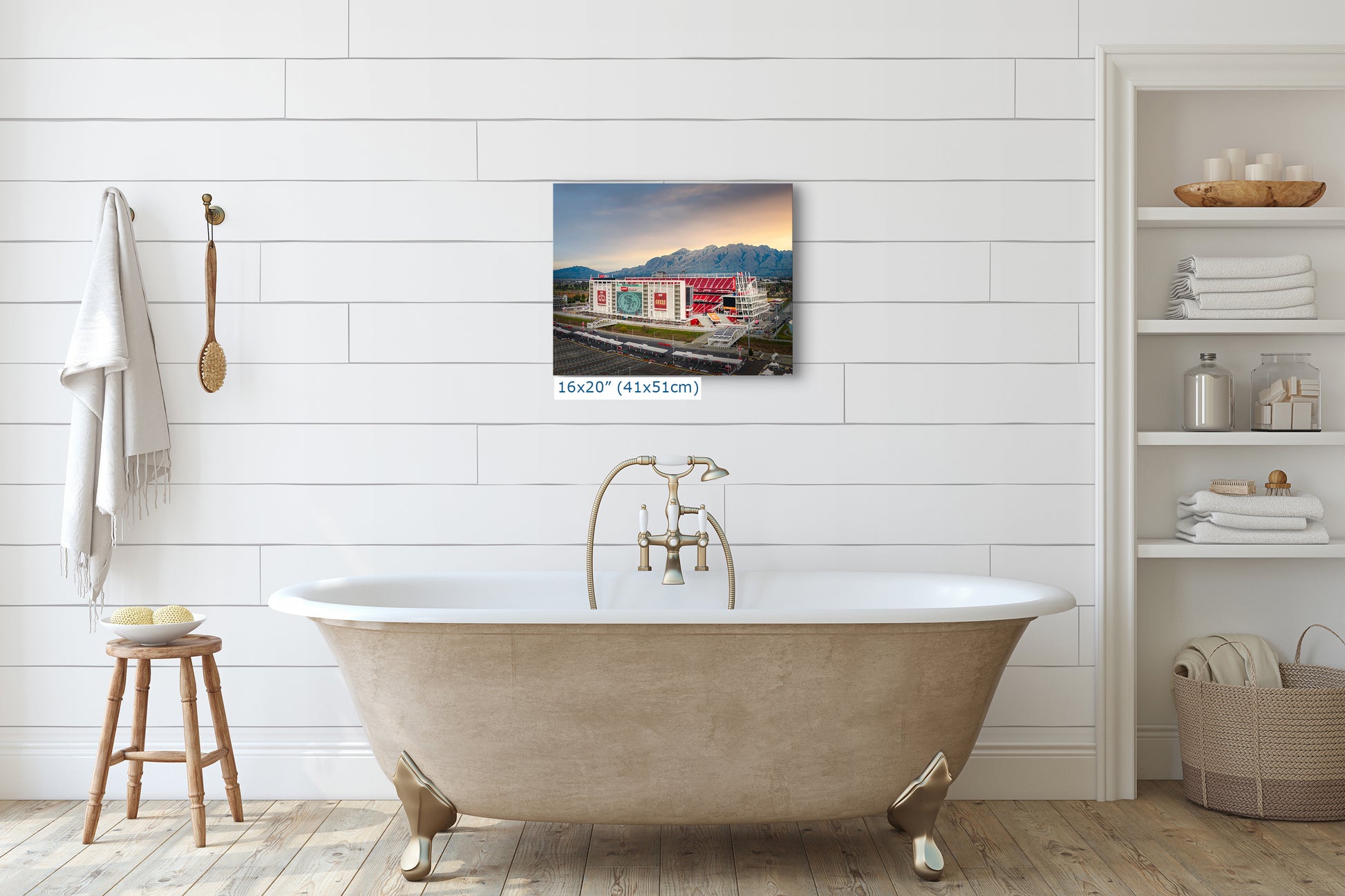a bathroom with a clawfoot bathtub, a wooden stool, and a shelf with various toiletries. Above the bathtub, there is a framed photograph of a building with a red roof and a mountain in the background.