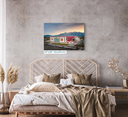 a bedroom with a bed, a wooden headboard, and a framed picture of a stadium on the wall above the bed.