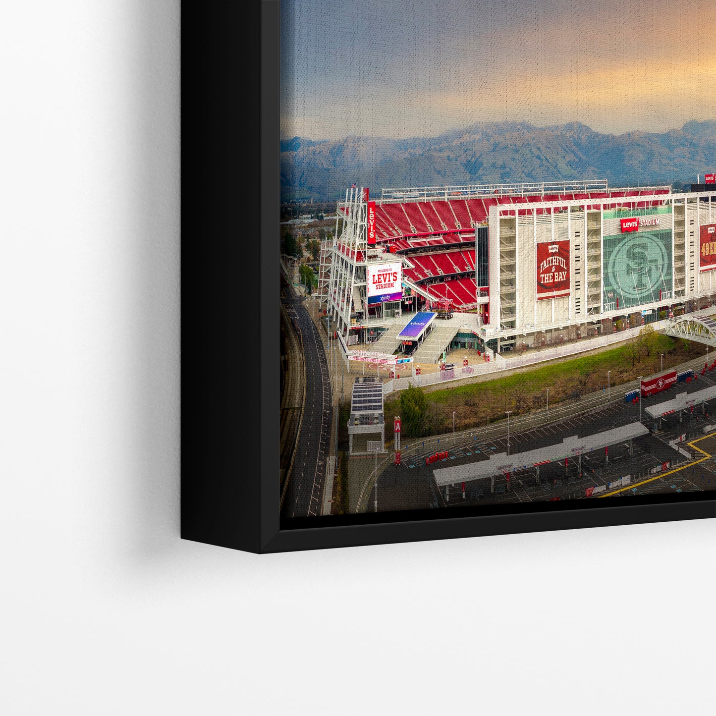 The image is a framed photograph of a large stadium with a mountain range in the background.