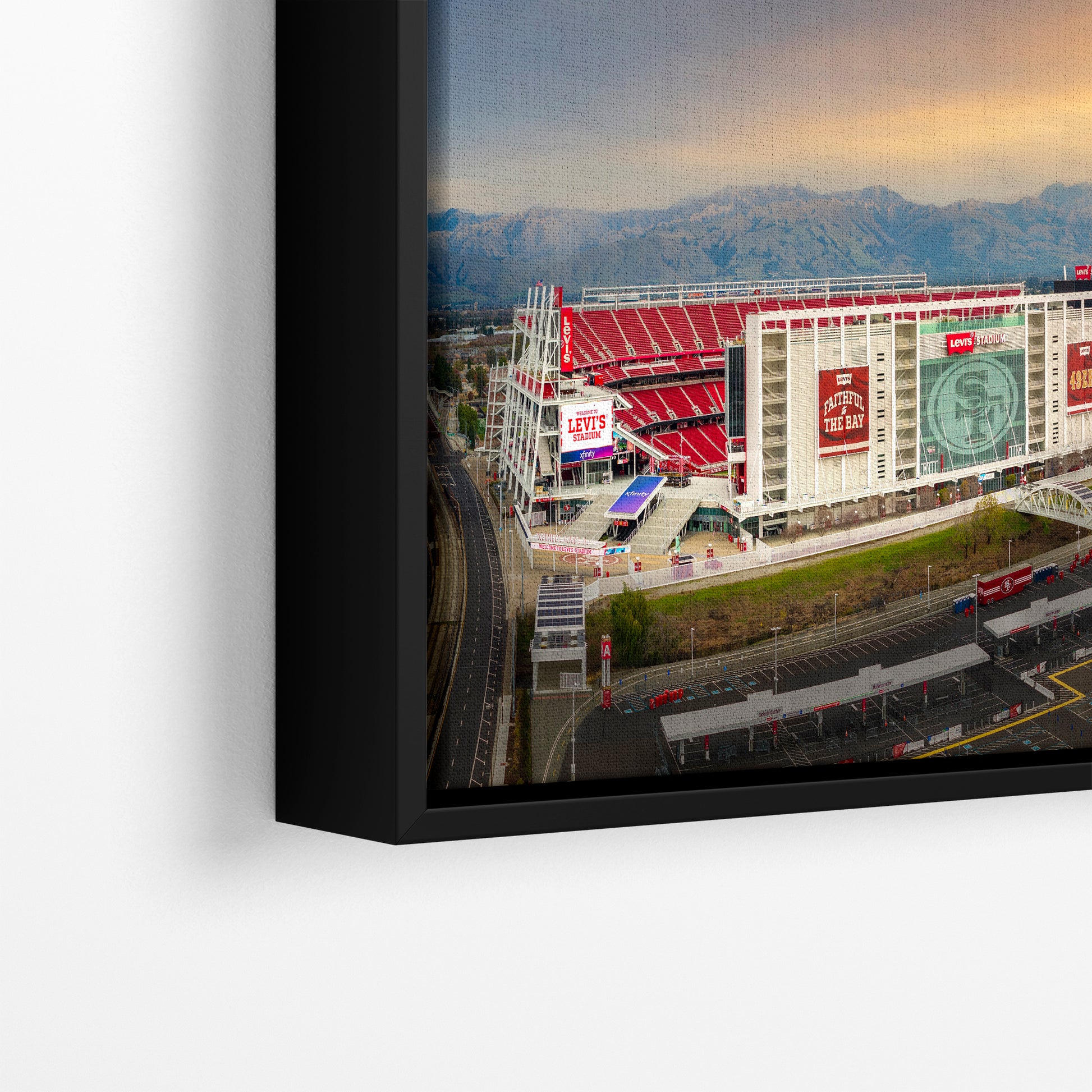 The image is a framed photograph of a large stadium with a mountain range in the background.