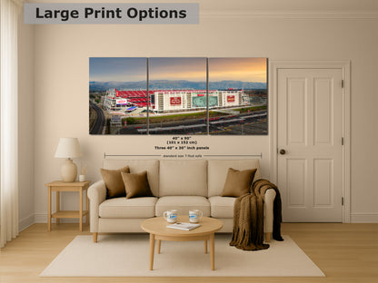 A large, three-panel print depicting a stadium with a red roof and white walls, set against a backdrop of mountains and a sunset sky.