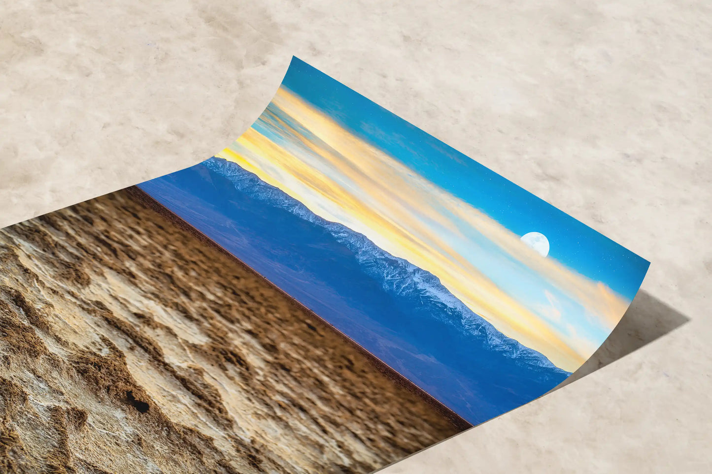 A paper print curving to reveal Death Valley's Badwater Basin under a sunset sky, captured in vivid colors and fine details.
