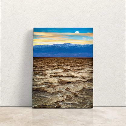 Front view of a canvas leaning against a wall featuring Death Valley's Badwater Basin salt flats with a sunset over the mountains.