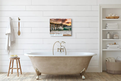 A 16x20 inch canvas print of Balboa Pier with a sunset backdrop, hung on a white shiplap wall above a clawfoot tub.