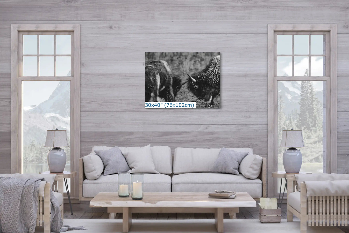 A 30x40 inch black and white canvas print of bison in combat, placed above a sofa in a cozy living room with a mountain view.