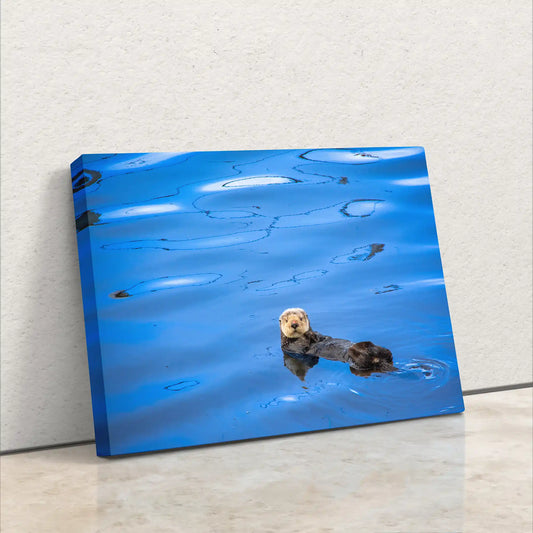 A side view of a canvas print leaning against a wall, showcasing the image of a sea otter adrift on calm blue waters.