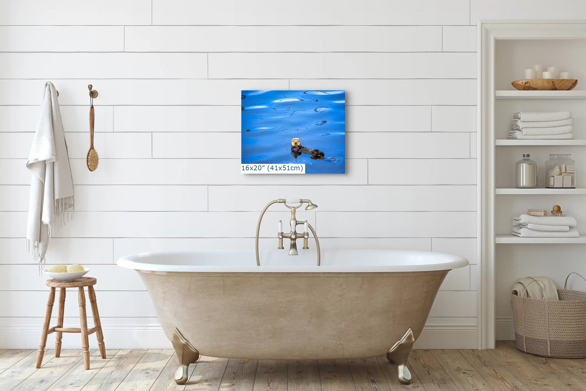 A 16"x20" canvas of a sea otter floating in blue water, hung on a white bathroom wall above a vintage bathtub.