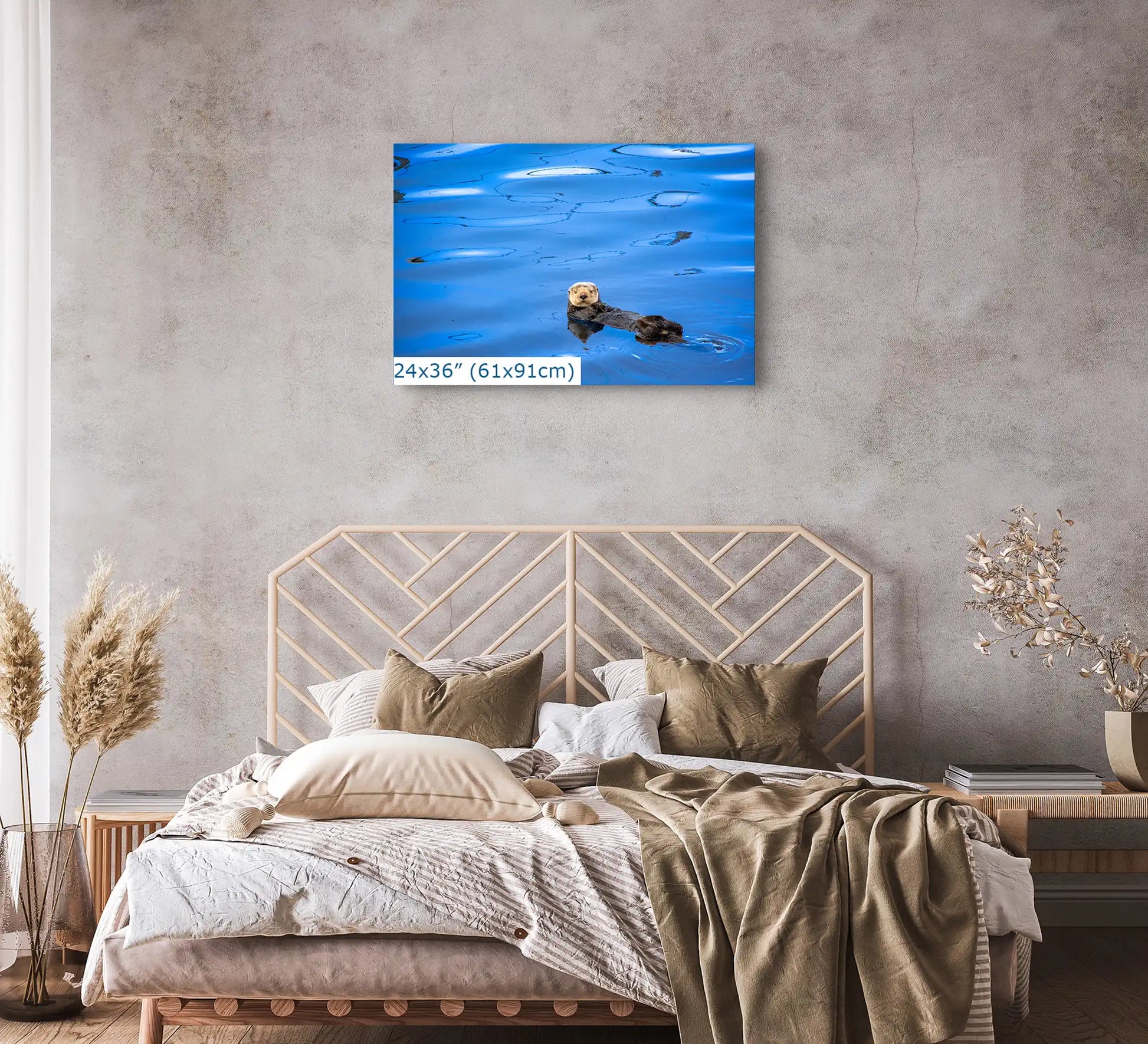 A 24"x36" wall art canvas featuring a sea otter, placed above a bed with neutral tones in a softly lit bedroom.