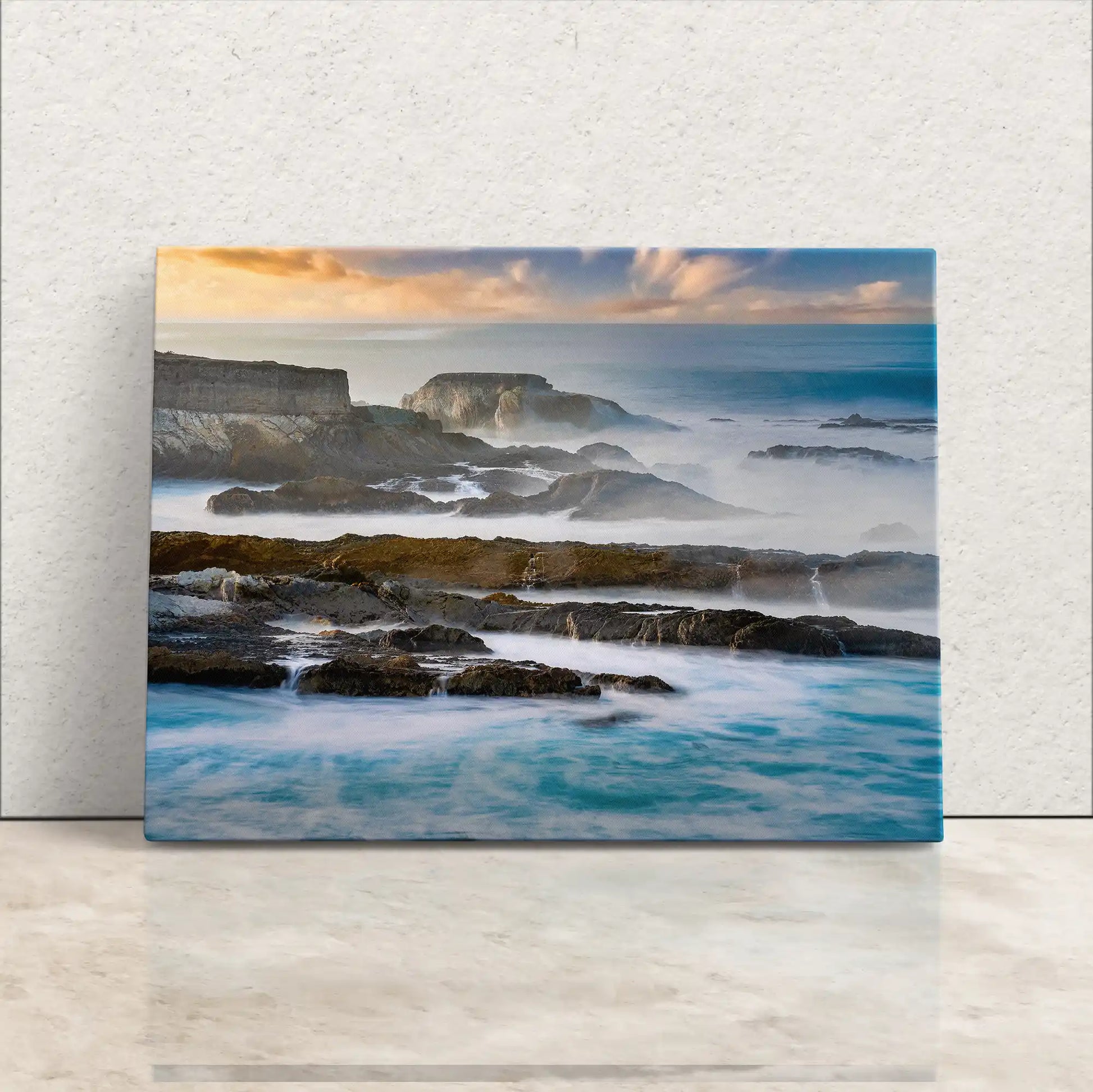Elegant canvas print leaning against a white wall, depicting the serene California Pacific coastline with its dramatic cliffs and misty ocean waves.
