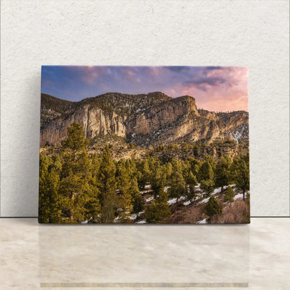 A canvas print of Fletcher Peak at Mt Charleston leans against a wall, showcasing a vivid portrayal of serenity, with lush pines under a radiant sunset sky, embodying tranquility and the artistry of nature.