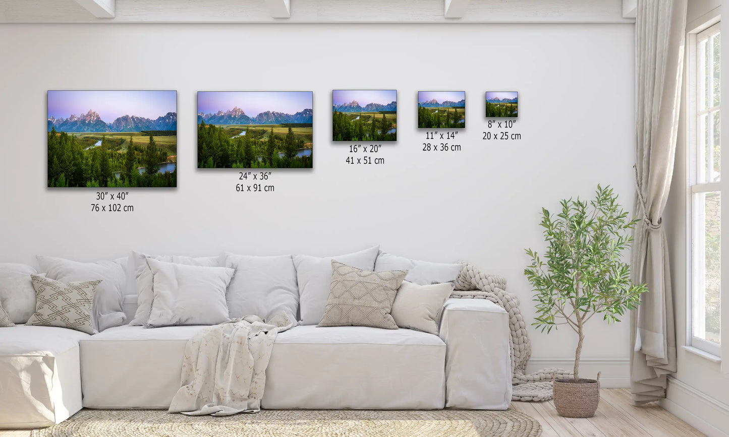 Various sized canvas prints of Grand Teton Mountains with a purple sunrise displayed above a sofa for size comparison.