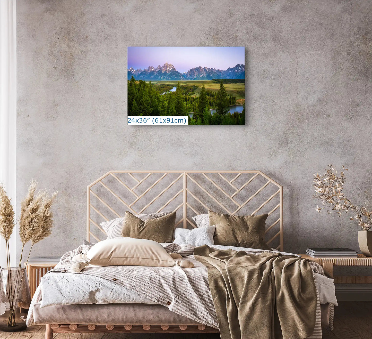 A 24x36 inch canvas print of Grand Teton Mountains during a purple sunrise on a bedroom wall above a bed with neutral bedding.