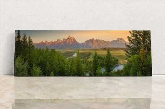 Frontal view of a panoramic wall art displaying the Teton Mountains and Snake River at sunrise, leaning against a wall.