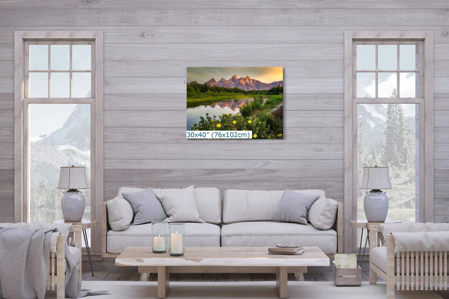 A large 30x40 inch canvas print on a living room wall, showing the Grand Teton Mountains at sunrise with reflective waters and wildflowers.