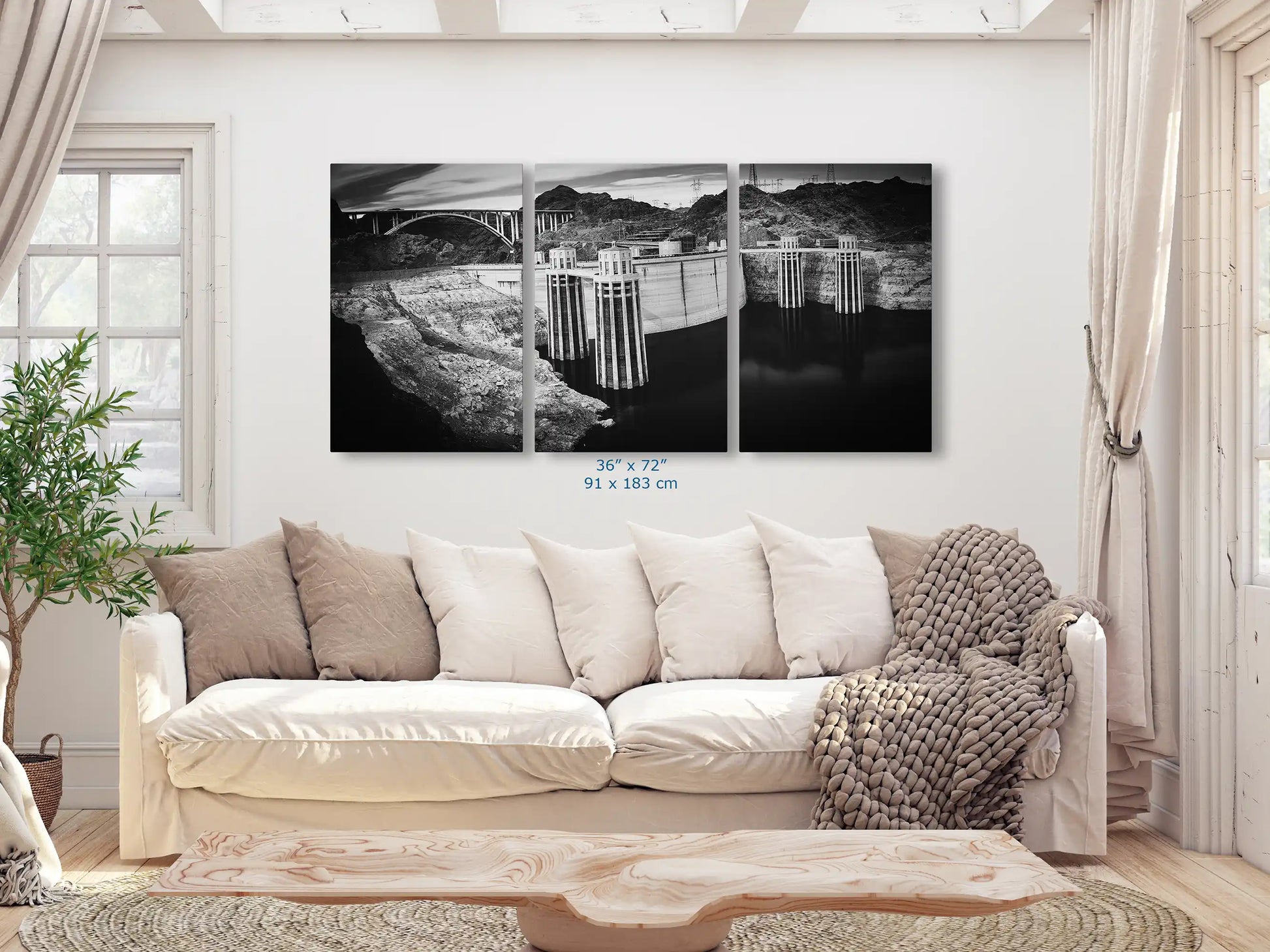 A black and white triptych canvas print of Hoover Dam, spanning 36x72 inches, dominates a living room wall with its impressive scale.