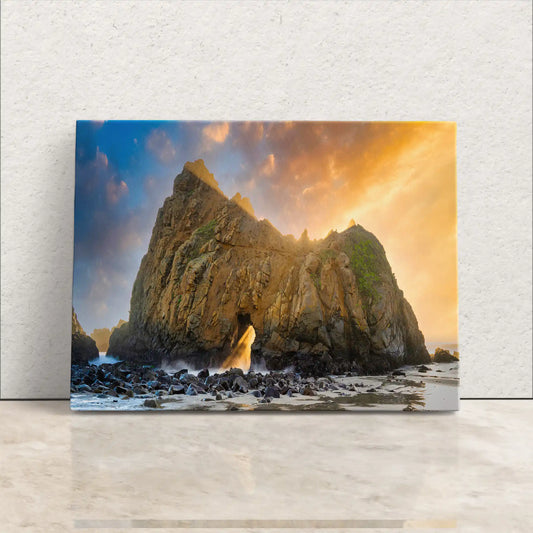 A canvas print leaning against a wall showing Keyhole Arch in Big Sur during sunset with vibrant orange skies and waves crashing through the rock.