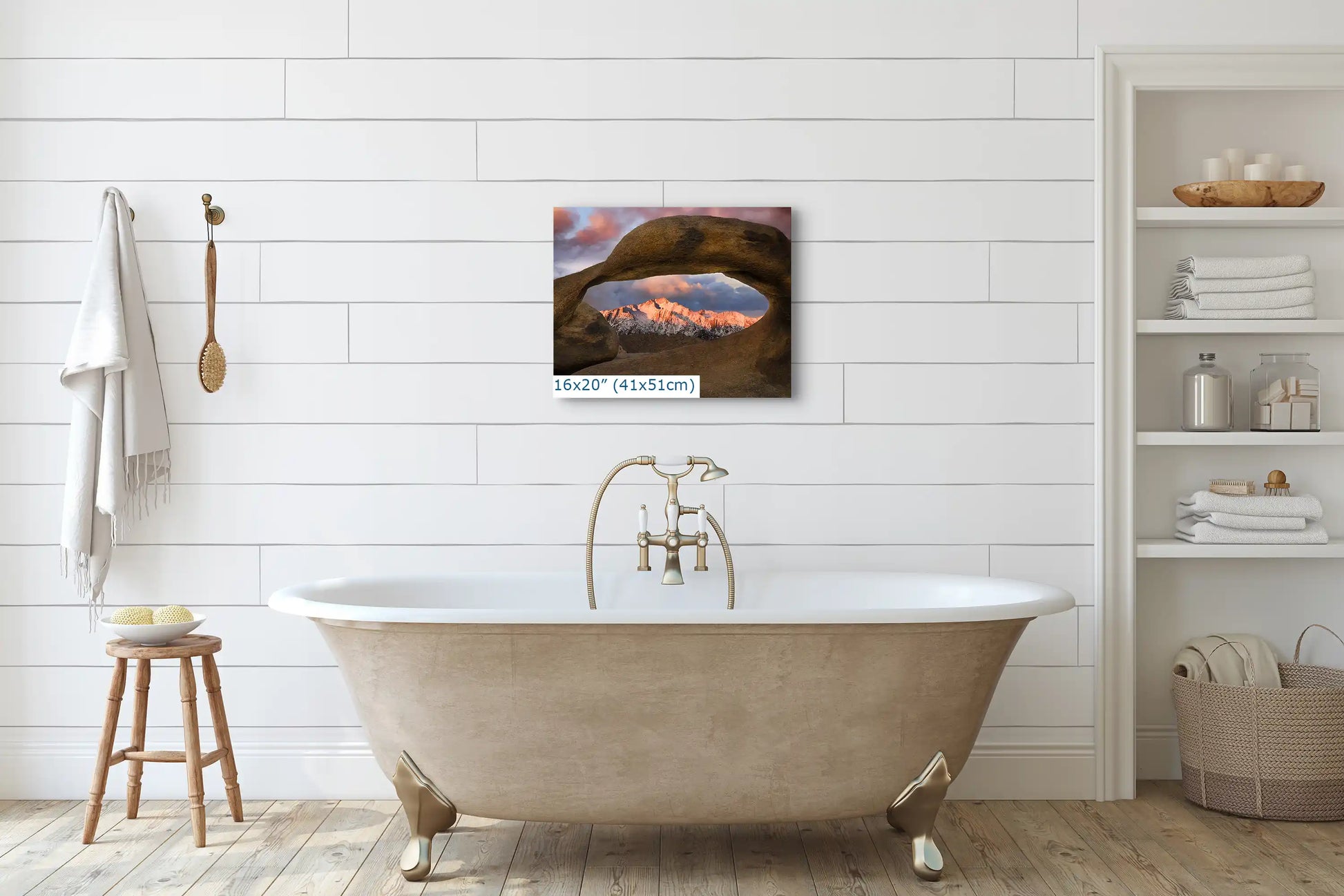 A 16x20 print of Lone Pine Peak through Mobius Arch hanging above a bathtub in a white-tiled bathroom.